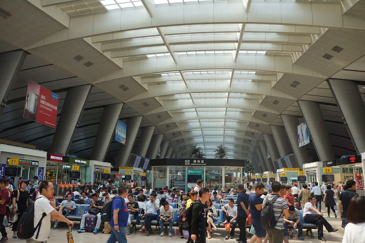 The vast waiting hall of Beijing South railway station under a curved roof, with crowds of passengers on benches and departure boards