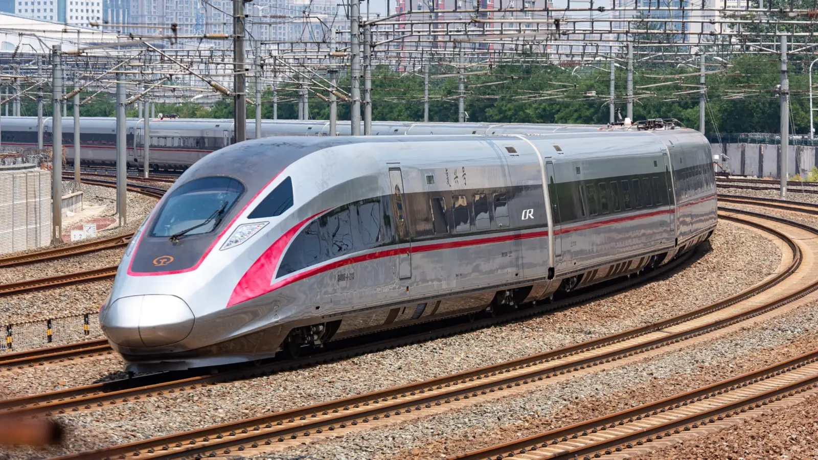 A silver Fuxing CR400AF high-speed train with a red stripe curving along the tracks near Beijing South station