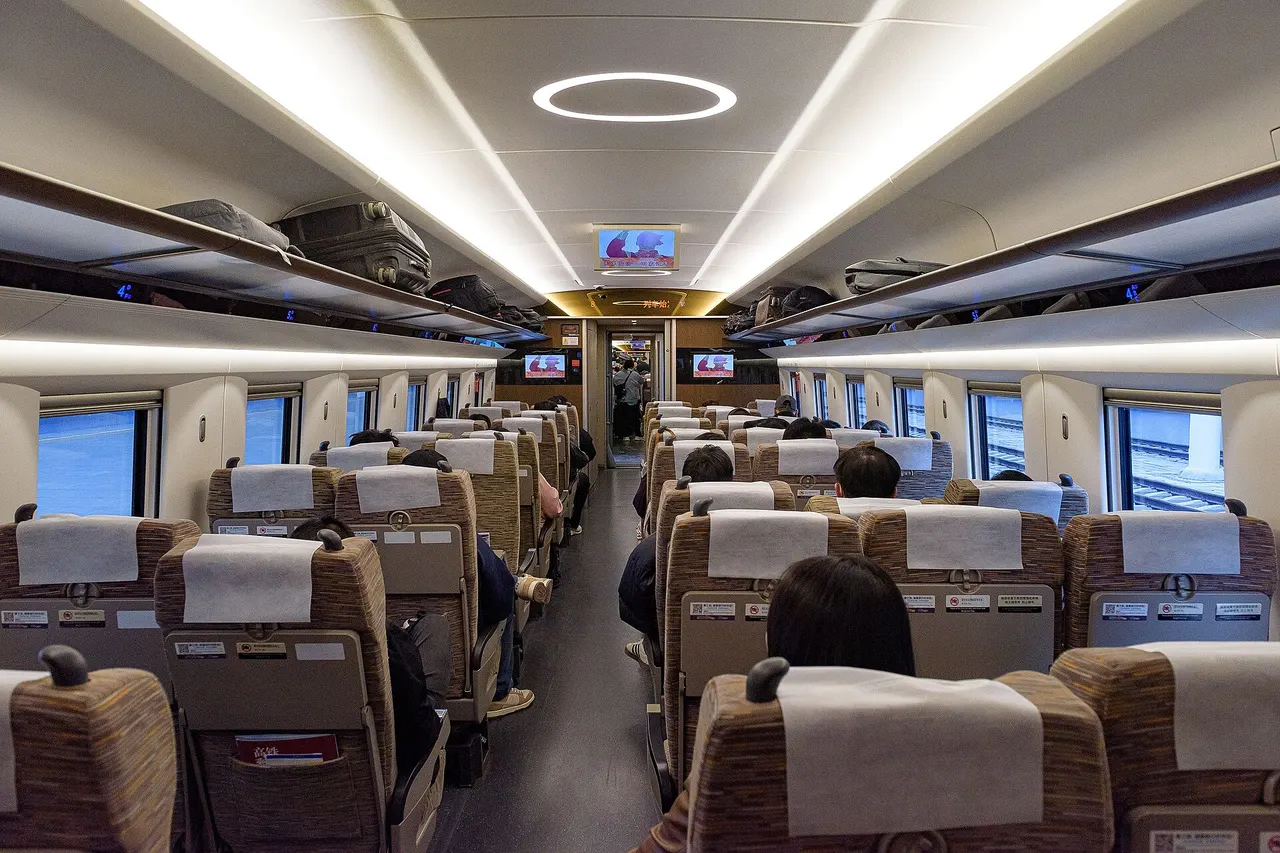 Second class carriage of a CR400AF train with rows of three and two fabric seats on either side of the aisle and passengers seated
