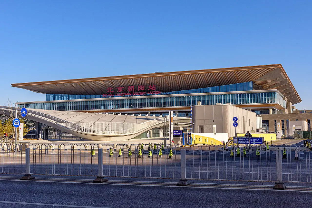The wide low roof of Beijing Chaoyang railway station with its red station name above a glass facade, under a blue sky