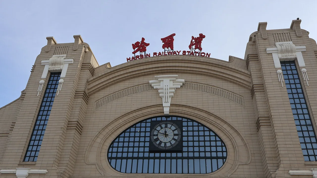 The cream-coloured Art Nouveau facade of Harbin Railway Station with a clock in the centre arch and the station name in red characters