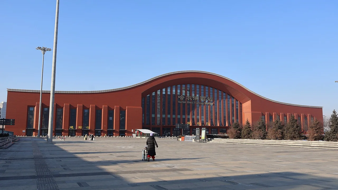 The red-brick arched facade of Harbin West railway station across an empty winter forecourt
