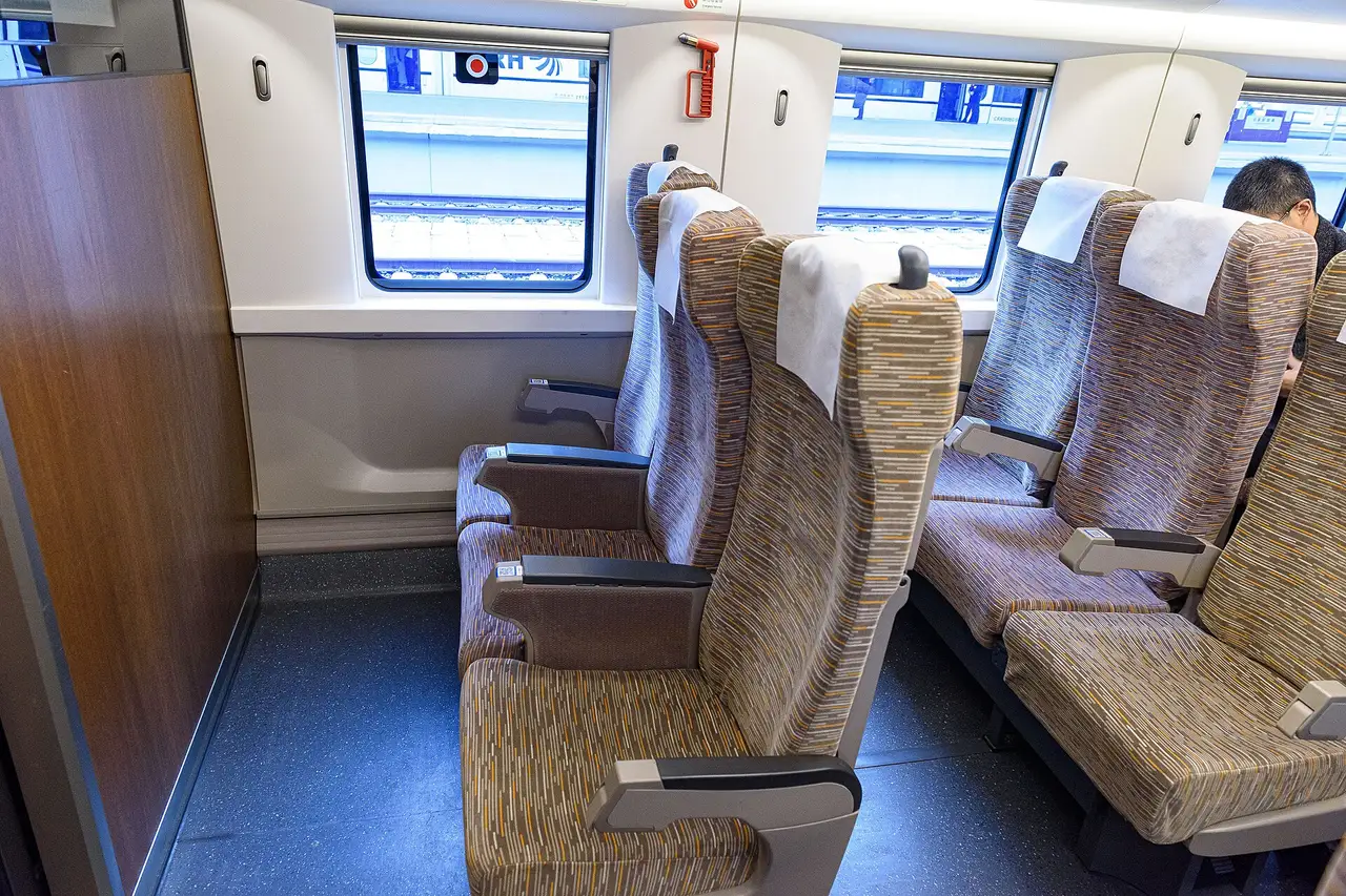 Rows of beige second-class seats in a high-speed train car, three seats on one side of the aisle and two on the other