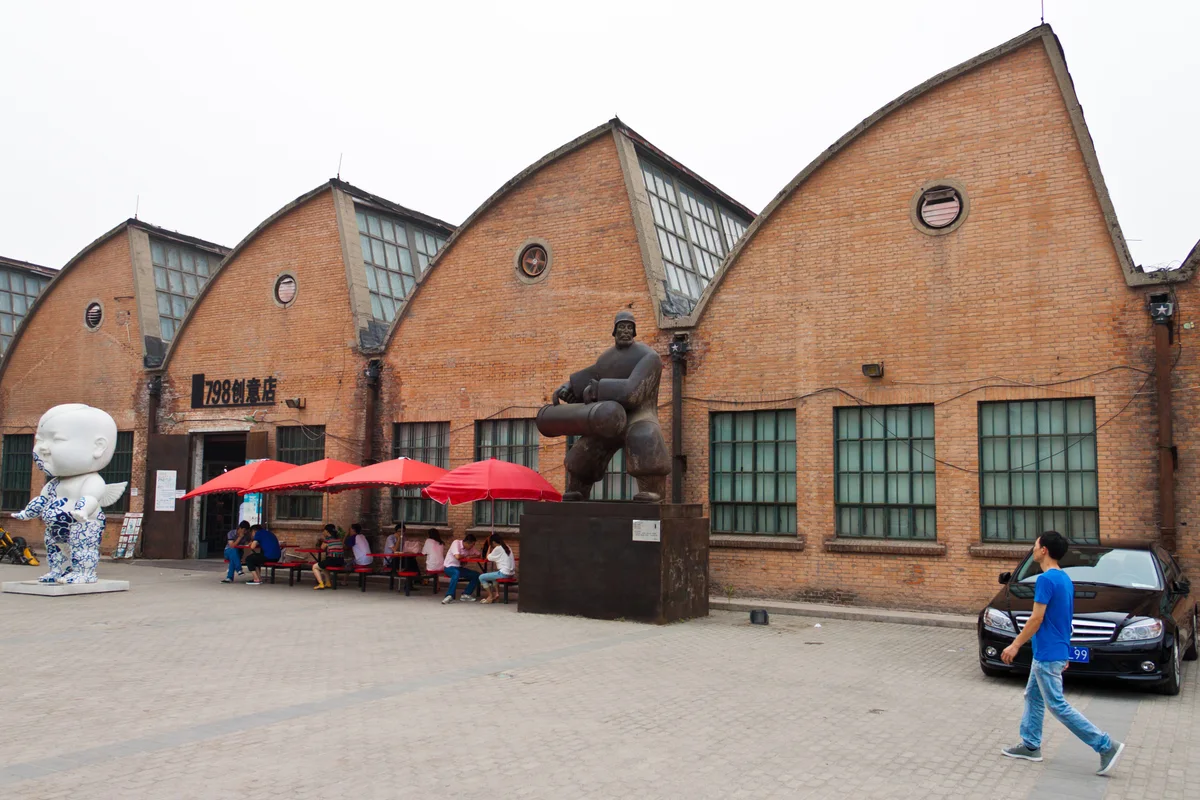 Red-brick factory halls with saw-tooth roofs and sculptures in the 798 Art Zone