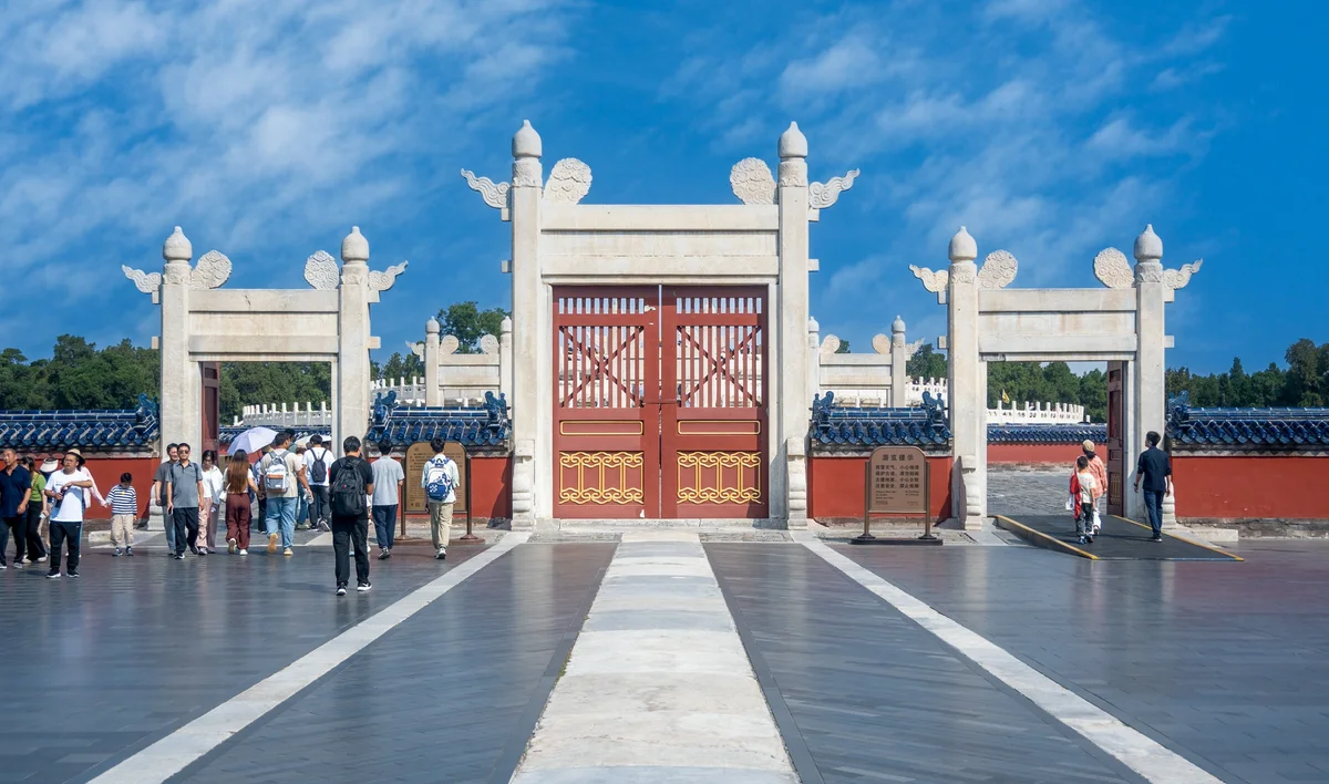 White marble gateways and a red door leading to the Circular Mound Altar at the Temple of Heaven, with visitors on the paved approach
