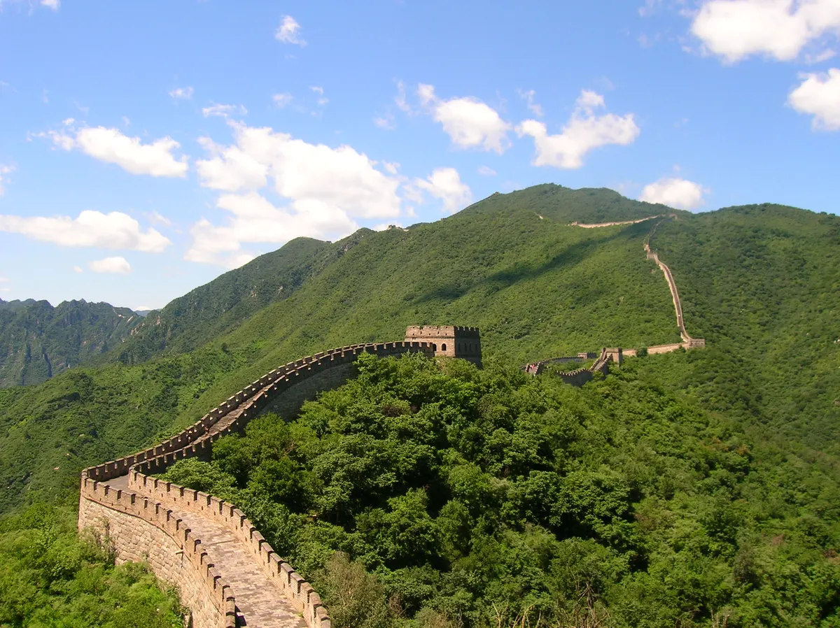 The Great Wall at Mutianyu snaking along green forested ridges under white clouds