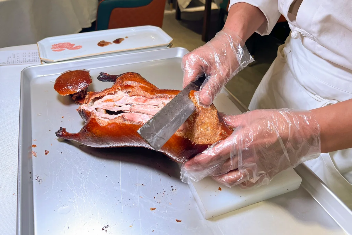A chef in gloves slicing the lacquered skin and meat of a roast duck on a carving board