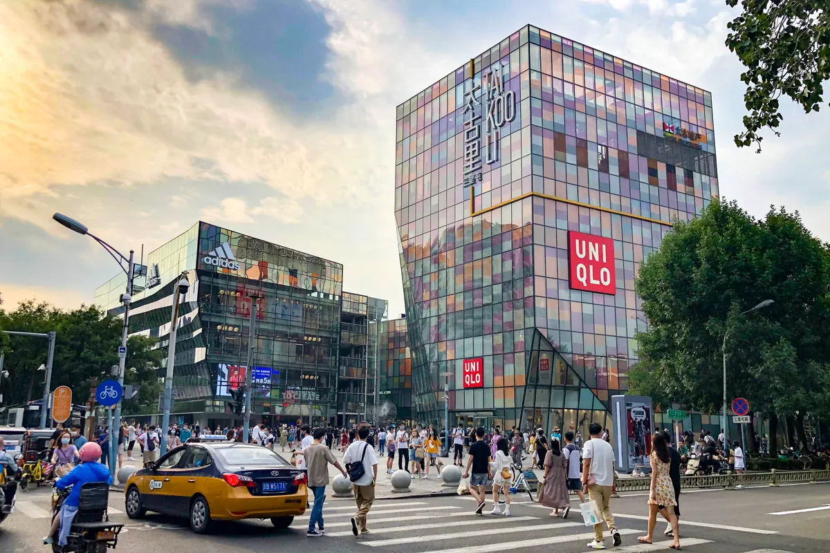 A crossroads in Sanlitun with a taxi, crowds of shoppers and the multicoloured glass buildings of Taikoo Li