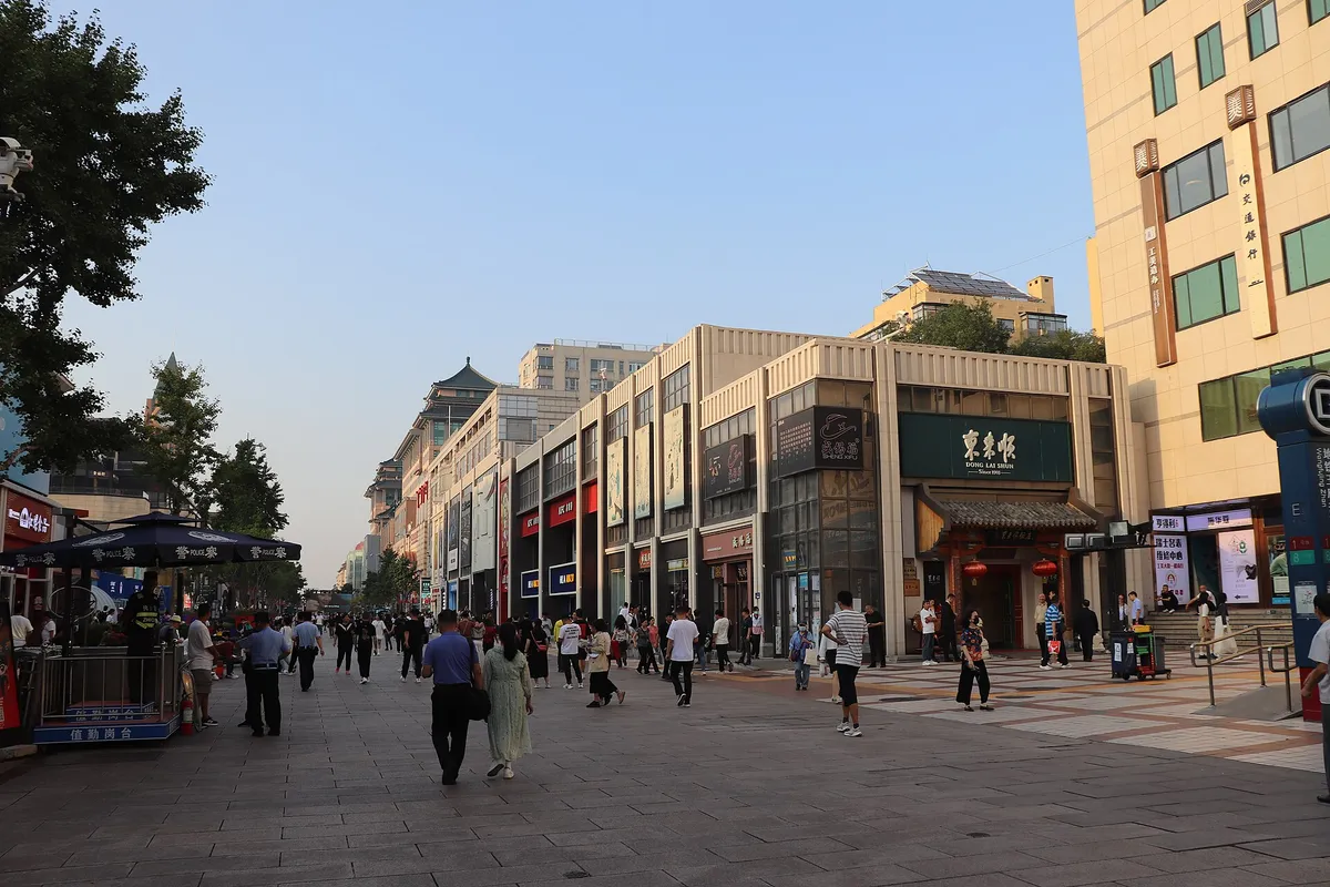 Shoppers walking the pedestrian stretch of Wangfujing street past shopfronts, one signed Dong Lai Shun, in early-evening light