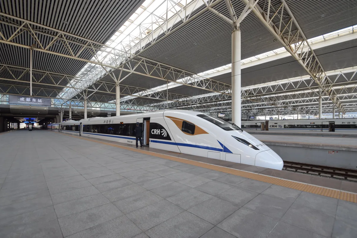 A white high-speed train with a blue stripe standing at a long platform under a steel-framed roof