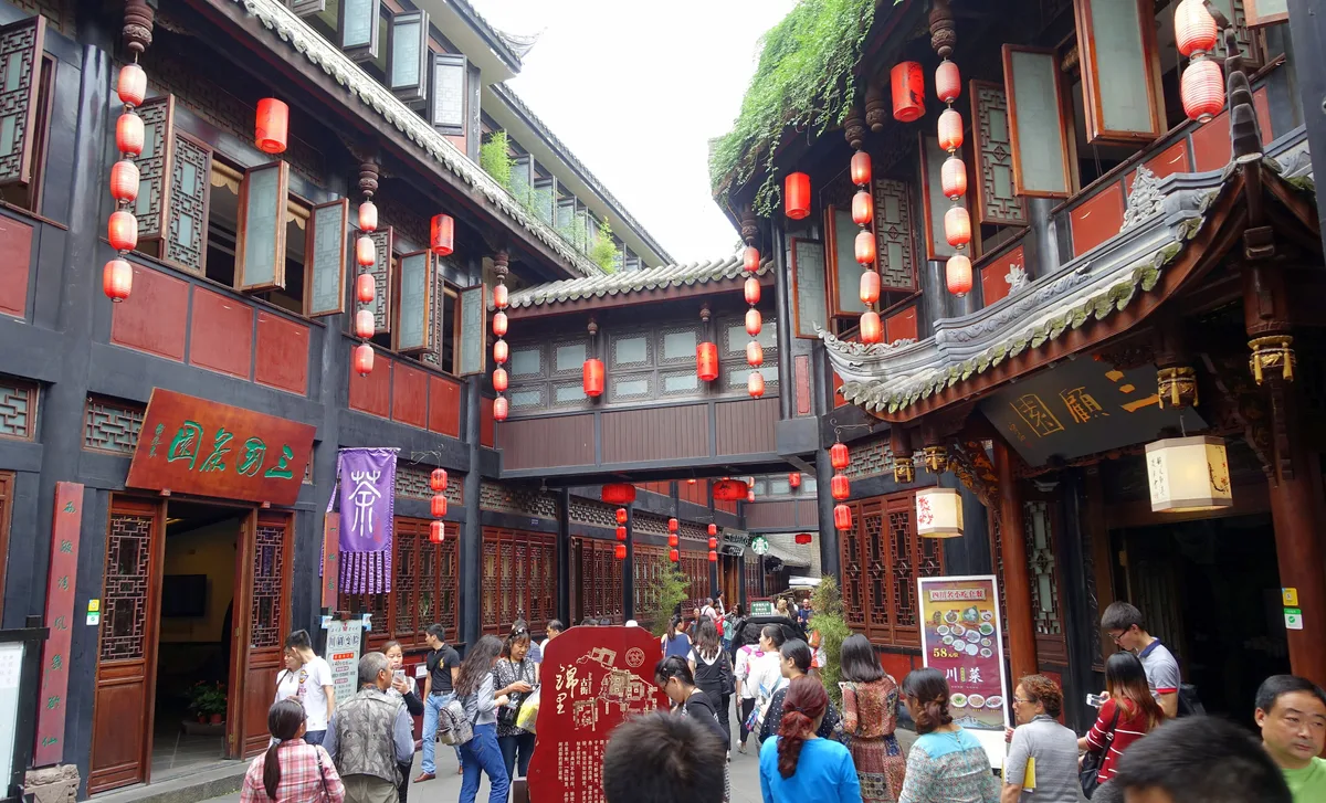 A crowded lane of dark wooden two-storey shopfronts hung with rows of red lanterns and shop signs in Chinese