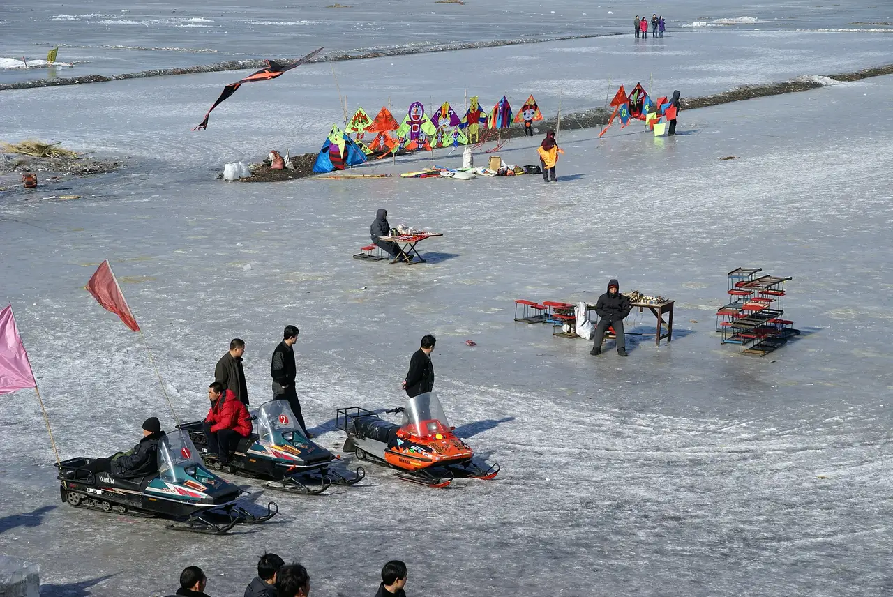 People, snowmobiles and colourful tents spread across the frozen surface of a wide river
