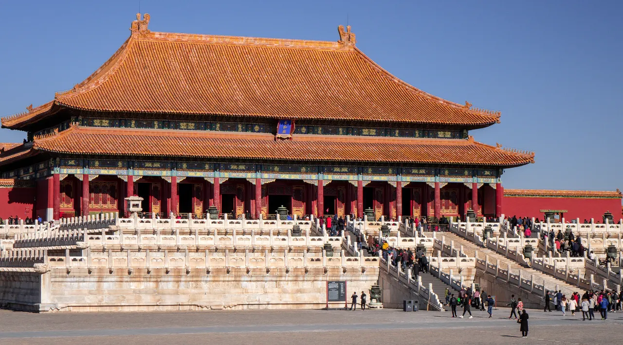 The Hall of Supreme Harmony in the Forbidden City, with its double yellow-tiled roof and red columns above three tiers of white marble terraces, visitors climbing the stairs