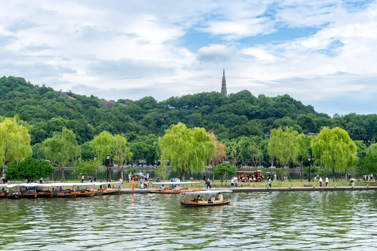 Rowing boats with white canopies on West Lake in Hangzhou, weeping willows along the shore and a slender pagoda on a wooded hill behind