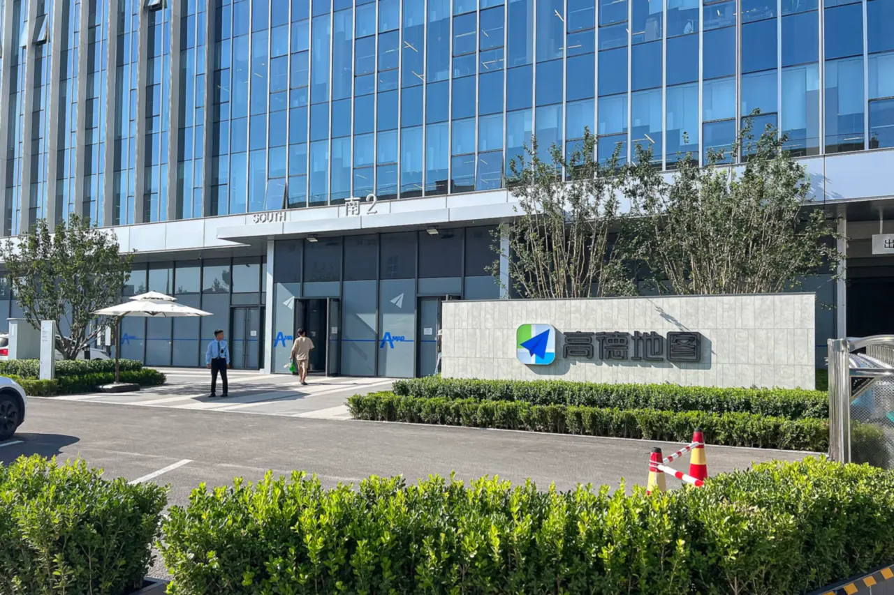 The south entrance of Amap's headquarters in Beijing, a glass office building with the blue Amap logo on a stone sign