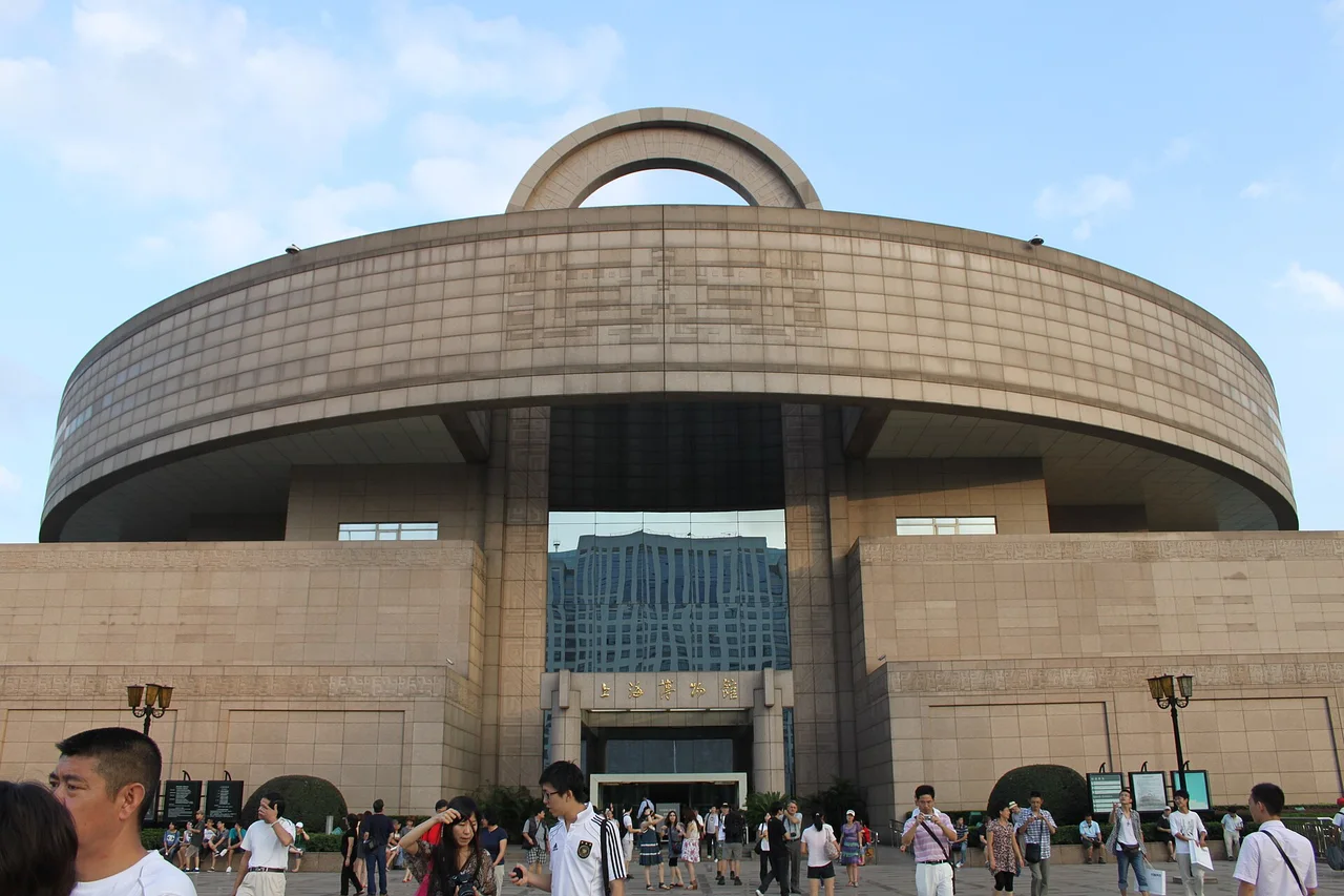 The round-topped stone building of the Shanghai Museum on People's Square with visitors and trees in front