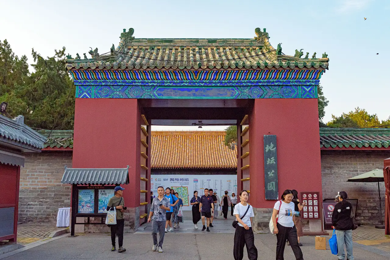 The red and blue painted south gate of Ditan Park in Beijing with visitors walking out beneath a green tiled roof