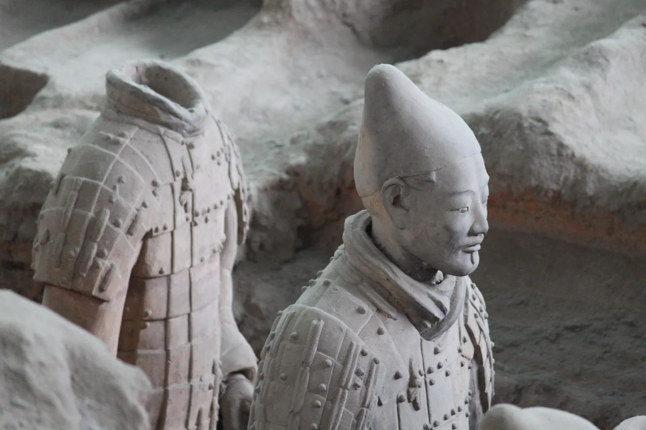 Close view of two terracotta warriors in Pit 1, one with a topknot cap and one headless, against the excavated earth