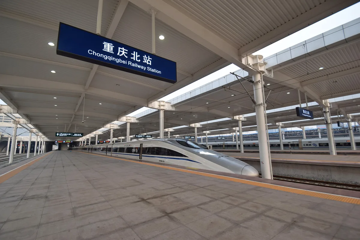 A white high-speed train at a long platform under a curved canopy, with a blue station sign hanging above