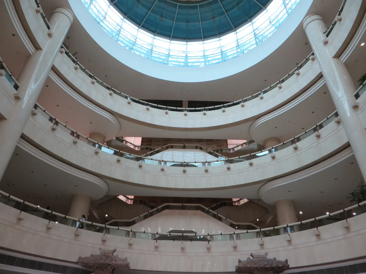 A round museum atrium with curved white galleries on several levels under a domed glass roof
