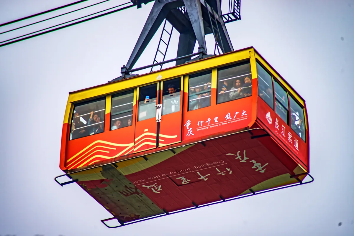 A red and yellow cable car cabin full of passengers hanging from its cable against a pale sky