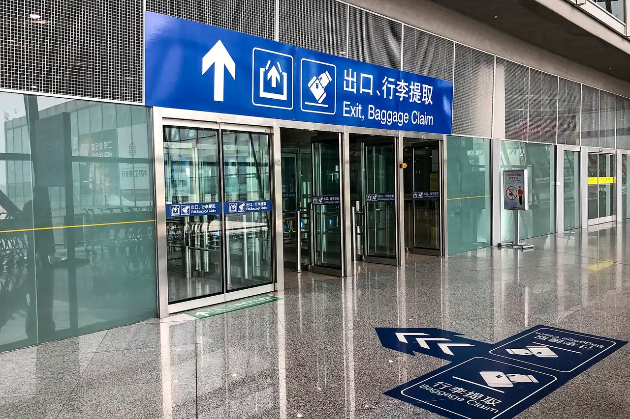 Glass exit doors under a blue Exit and Baggage Claim sign in the arrivals concourse of Beijing Capital airport Terminal 3