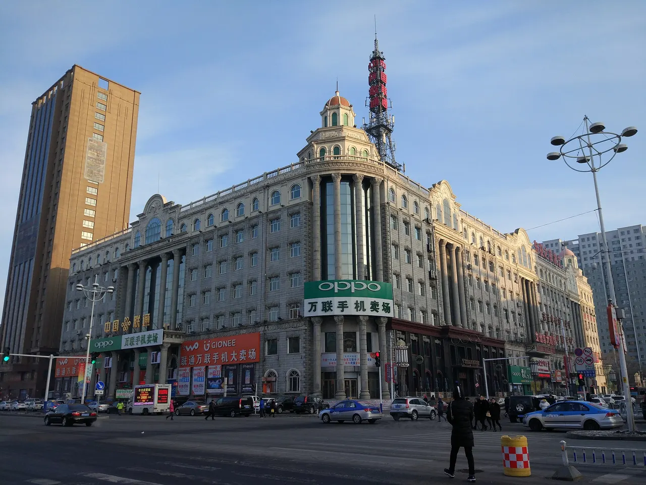 A large ornate building housing China Unicom's central business hall in Jiamusi, with a telecom tower on the roof and traffic in front