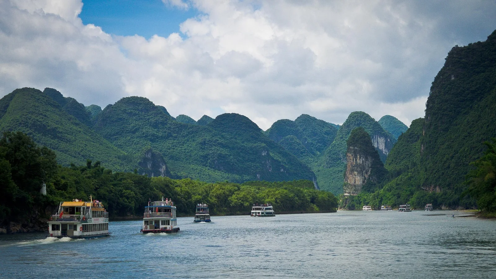 Tourist boats on the Li River near Guilin between steep green karst peaks under a cloudy sky