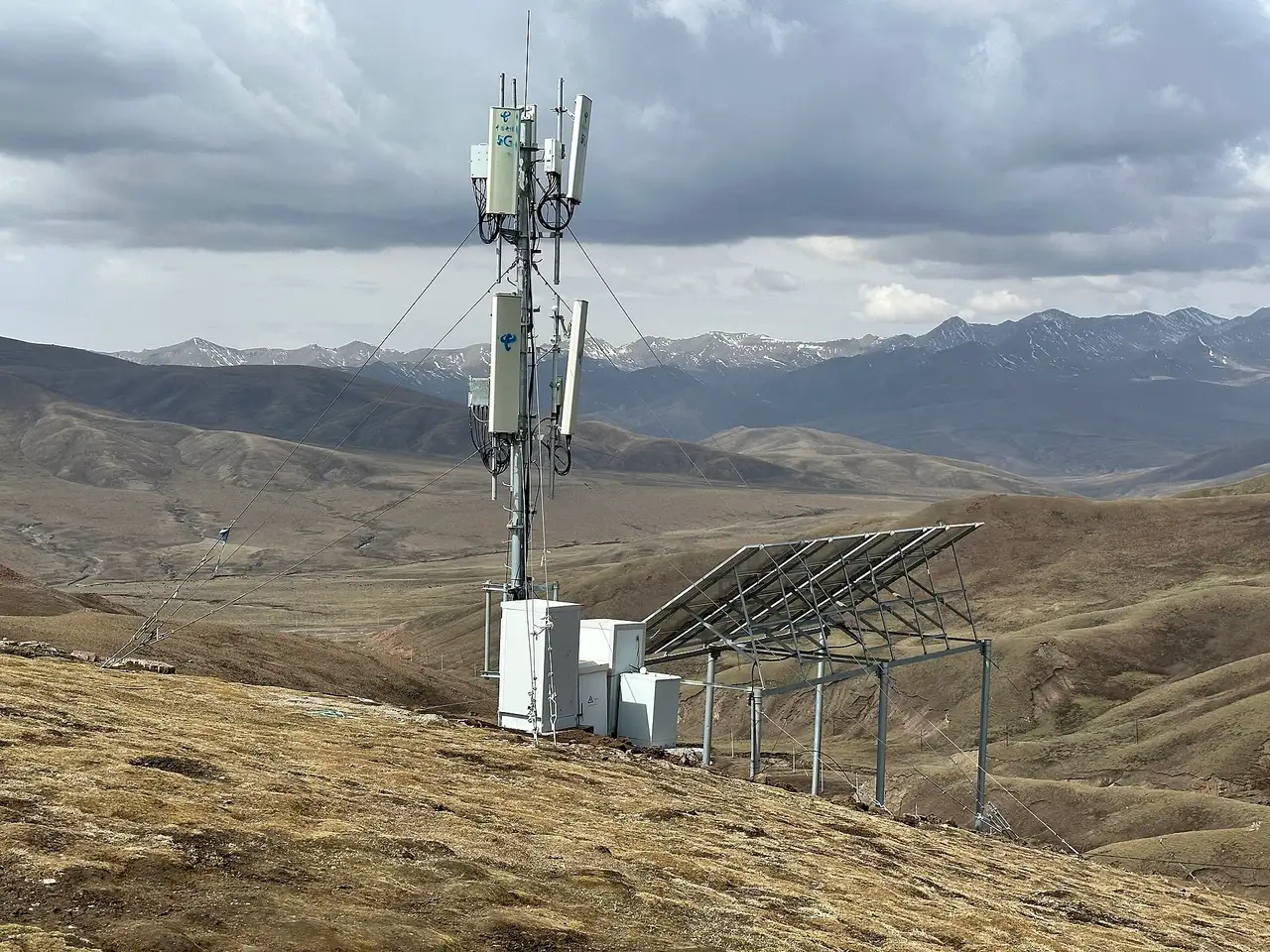 A 5G mobile mast with solar panels on a bare hillside at the Laji Mountain pass in Qinghai, with brown mountains behind