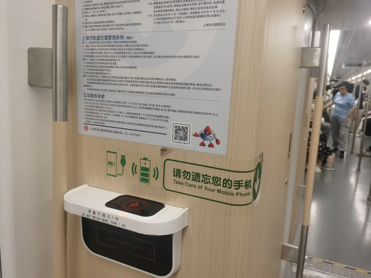 A wireless phone charging pad on the wall of a Shanghai Metro carriage with a green sign reading Take Care of Your Mobile Phone