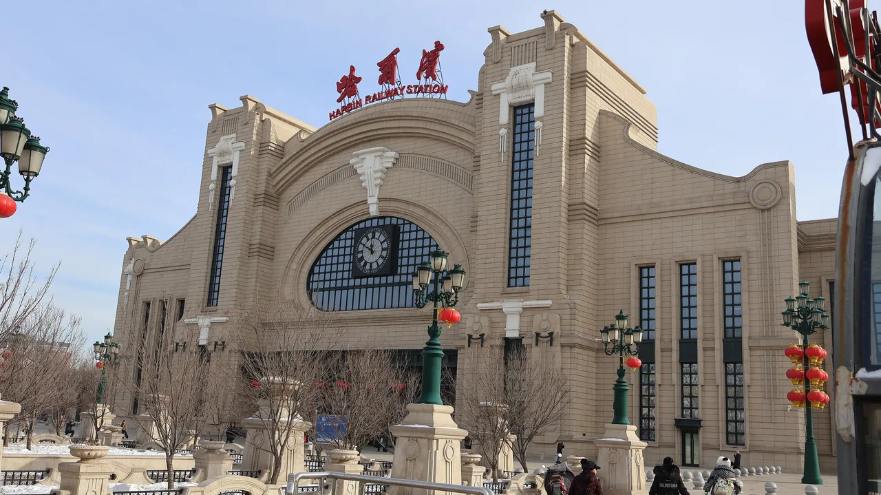 The stone facade of Harbin Railway Station with its large clock and red lanterns on the lamp posts, in winter