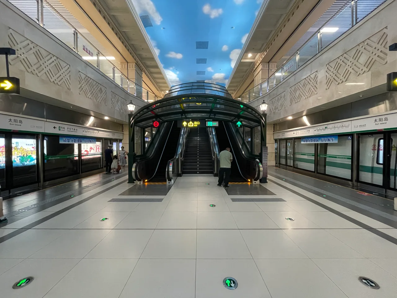 A Harbin Metro Line 2 station with a blue sky ceiling, escalators and platform screen doors