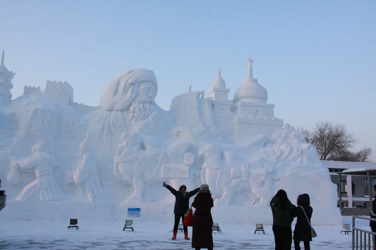 A large white snow sculpture of a building facade with two people standing beside it under a blue sky