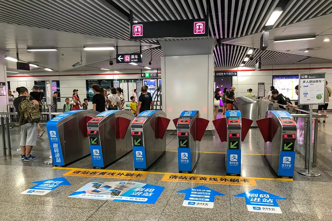 A row of blue metro faregates with QR code readers and Alipay markings at Ding'an Road station in Hangzhou