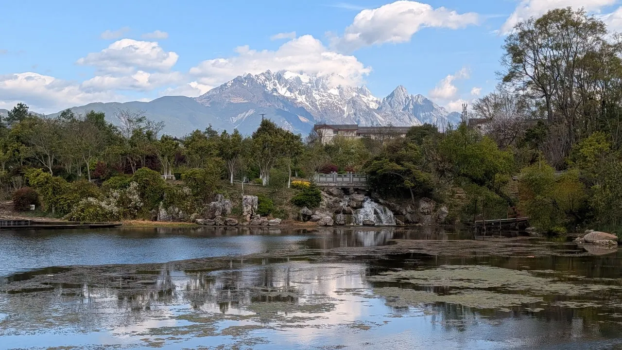 The snow-capped peaks of Jade Dragon Snow Mountain above wooded hills, reflected in the still water of Black Dragon Pool in Lijiang