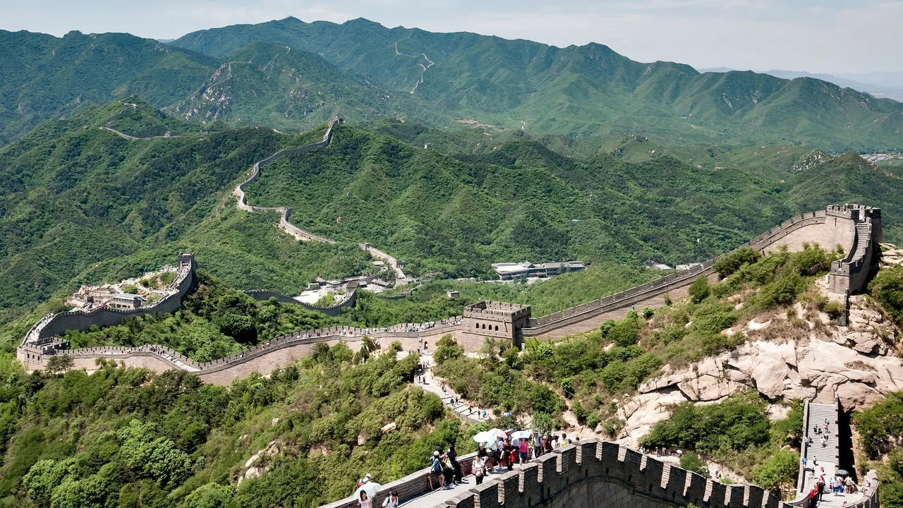 The Great Wall at Badaling running along green ridges, with a watchtower in the middle and visitors walking the ramparts in the foreground