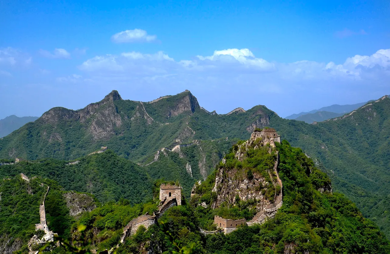 Unrestored towers of the Great Wall at Jiankou on steep, forested peaks under a blue sky