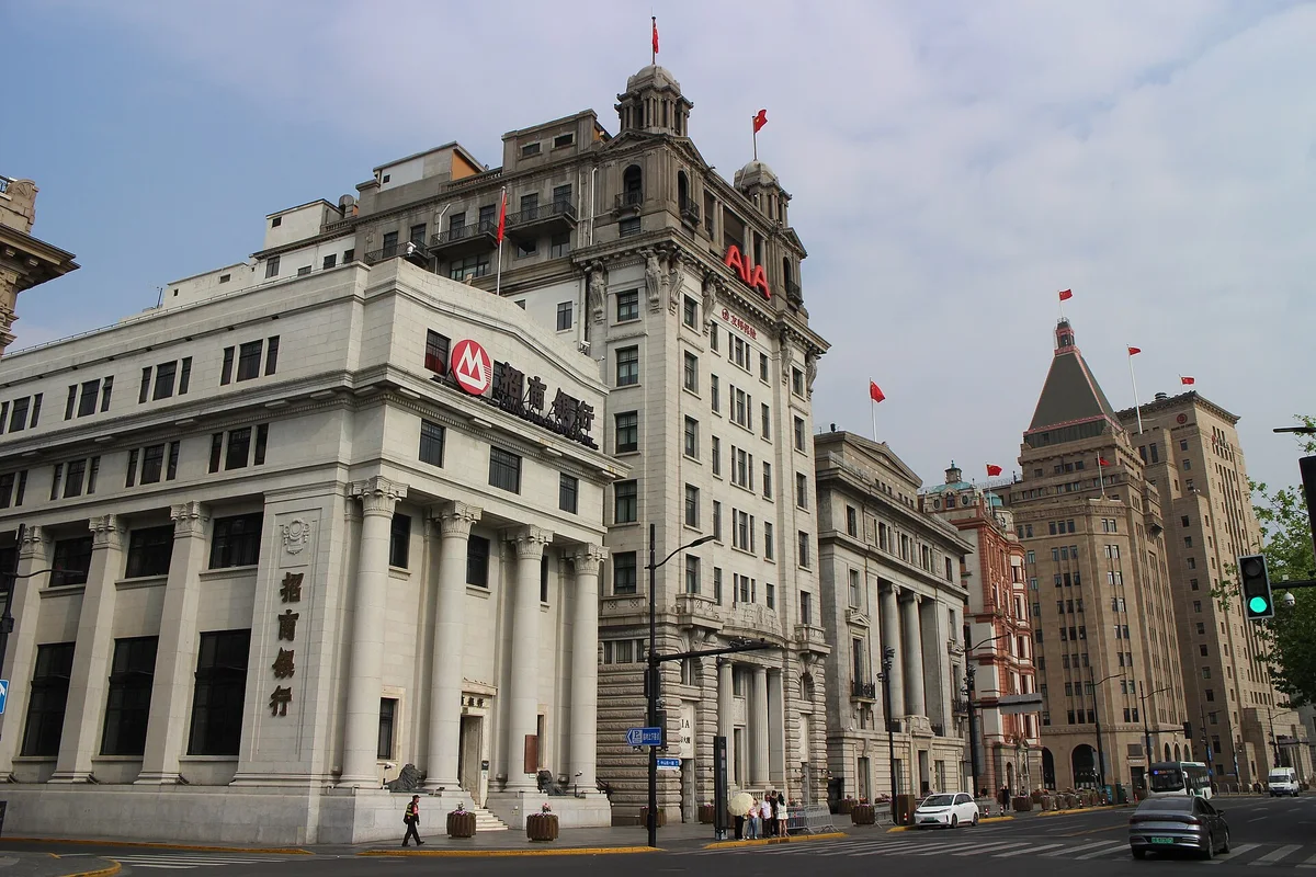 Colonnaded stone bank buildings and a domed office block along a quiet street on the Bund under a grey morning sky