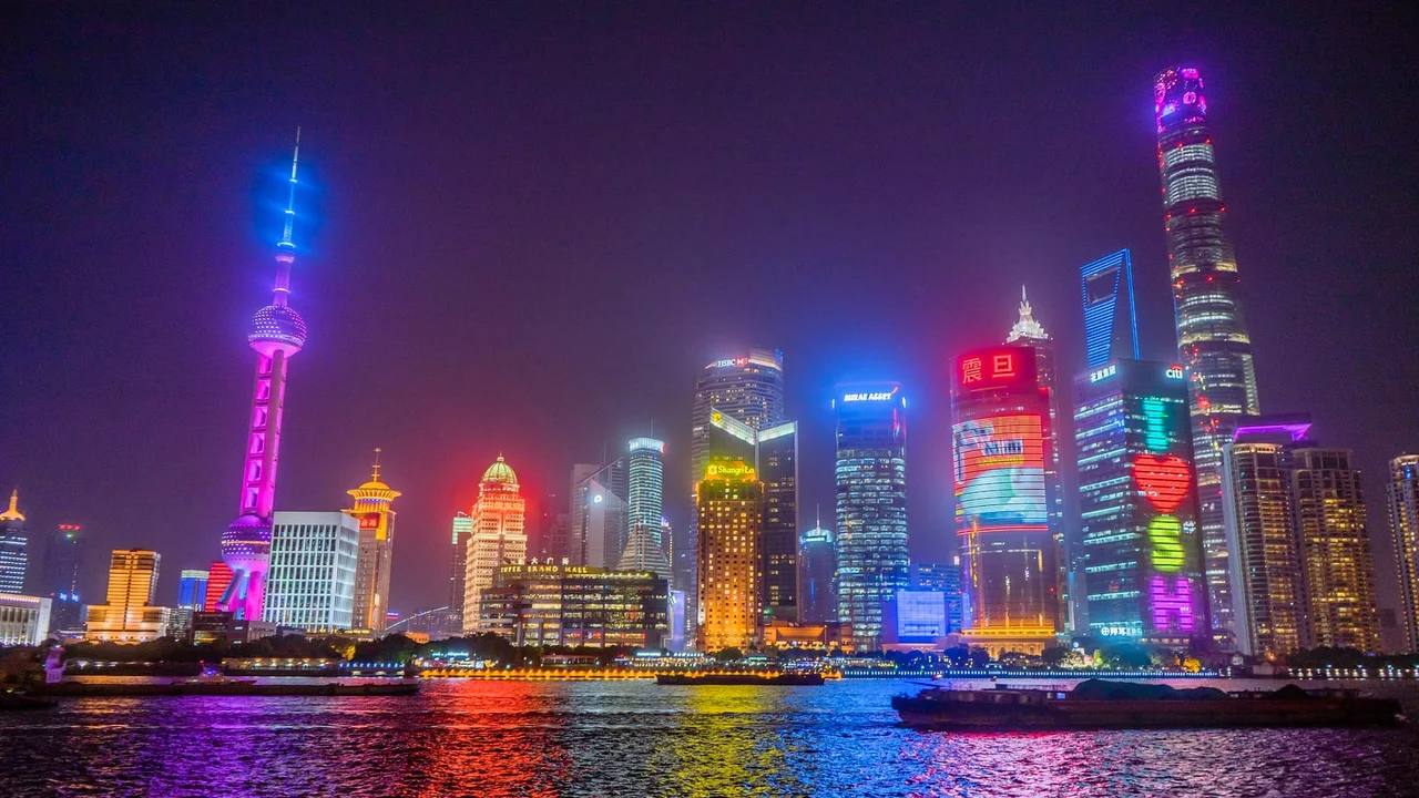 The Lujiazui skyline lit up at night across the Huangpu River, with the Oriental Pearl Tower glowing violet on the left and the Shanghai Tower on the right