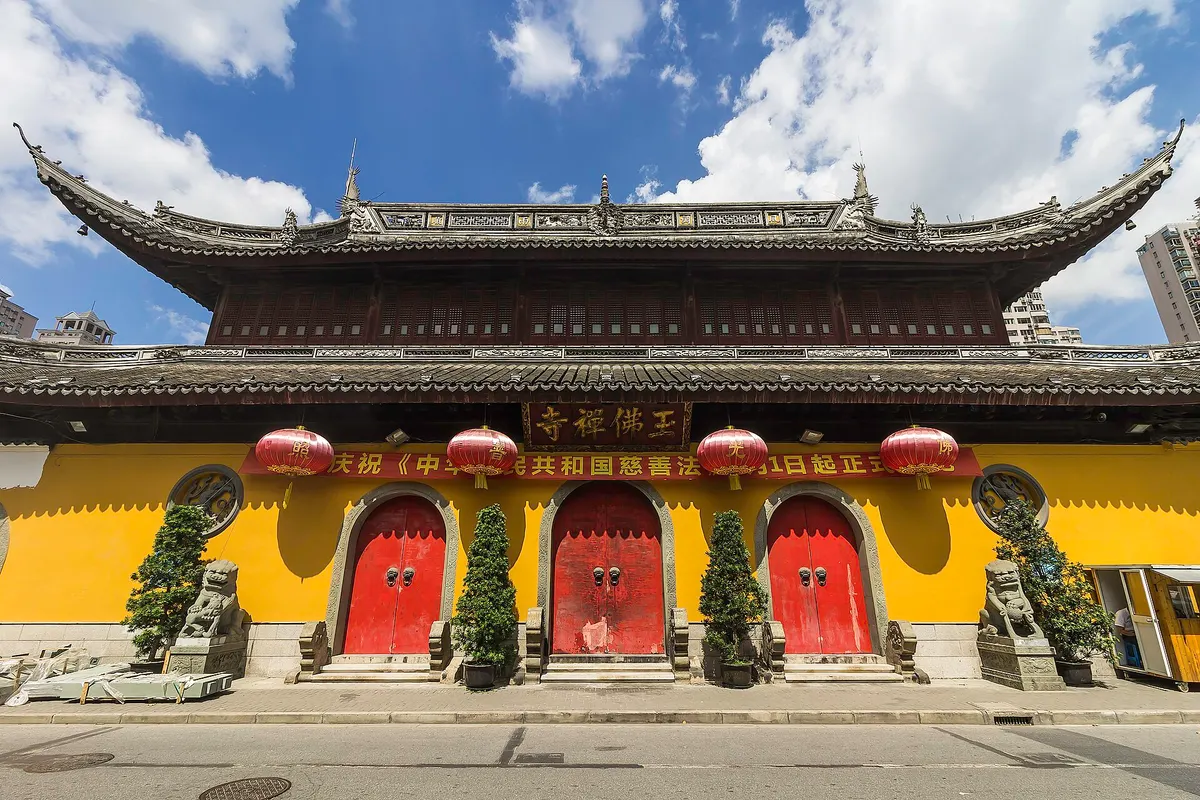 The yellow-walled front hall of the Jade Buddha Temple with three red doors, red lanterns and clipped pines