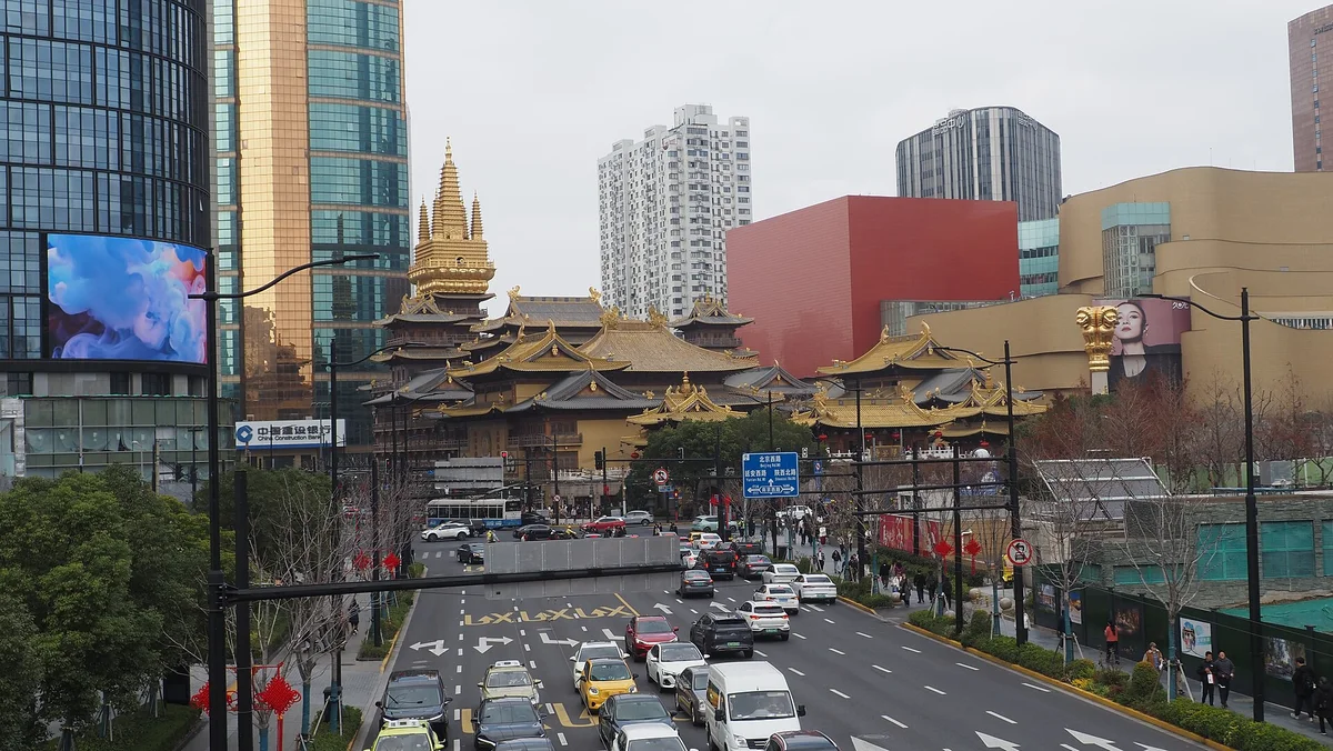 The gilded roofs of Jing'an Temple between glass office towers above a busy multi-lane road