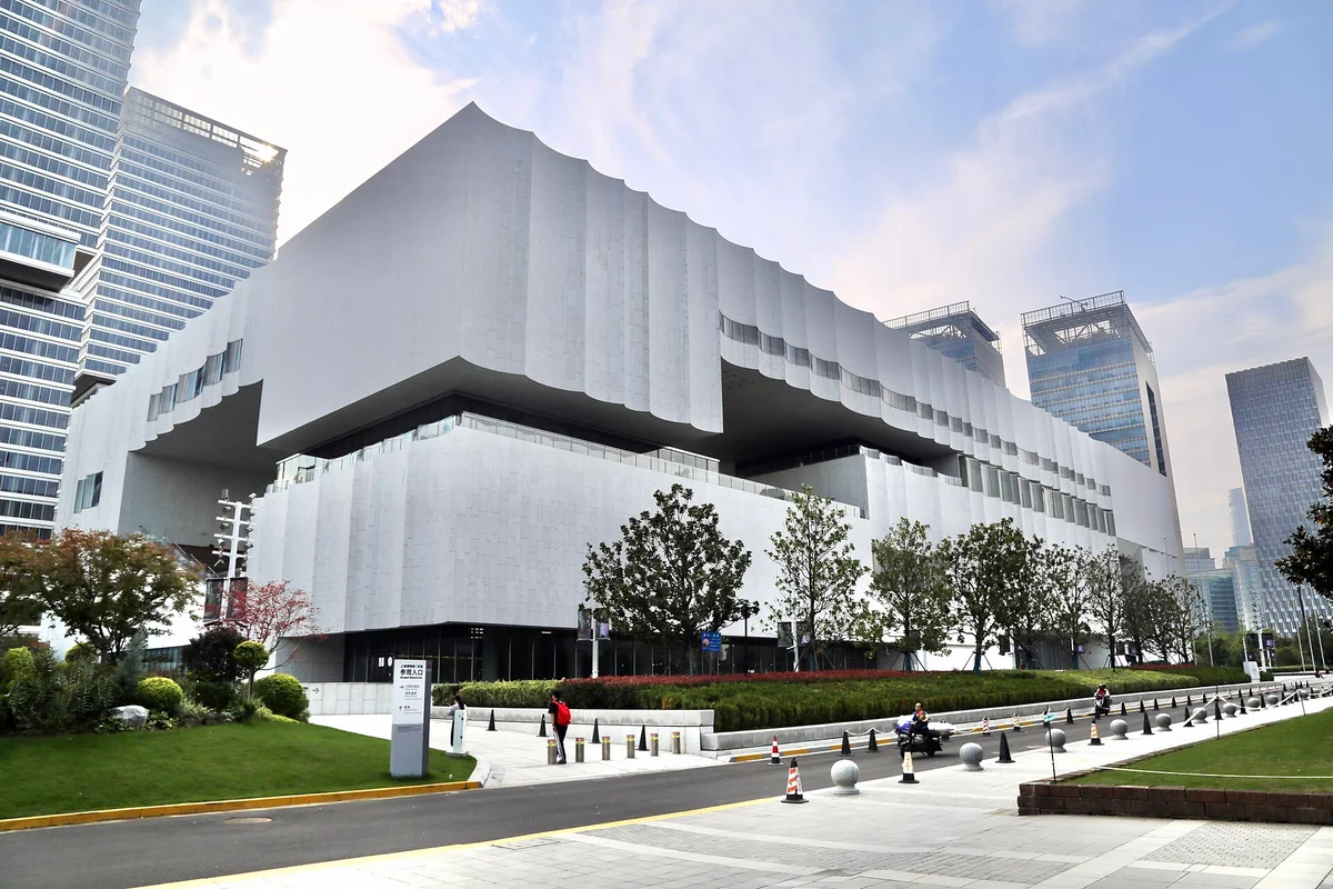 The white, stacked blocks of the Shanghai Museum East building beside a wide avenue, with office towers behind