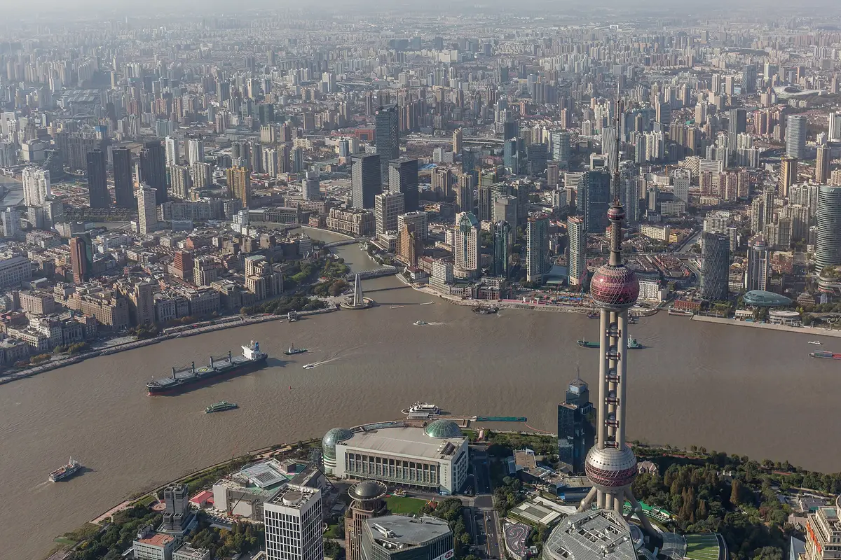 View down from the Shanghai Tower over the Oriental Pearl Tower, a bend of the Huangpu River with ships and the dense city beyond in afternoon haze