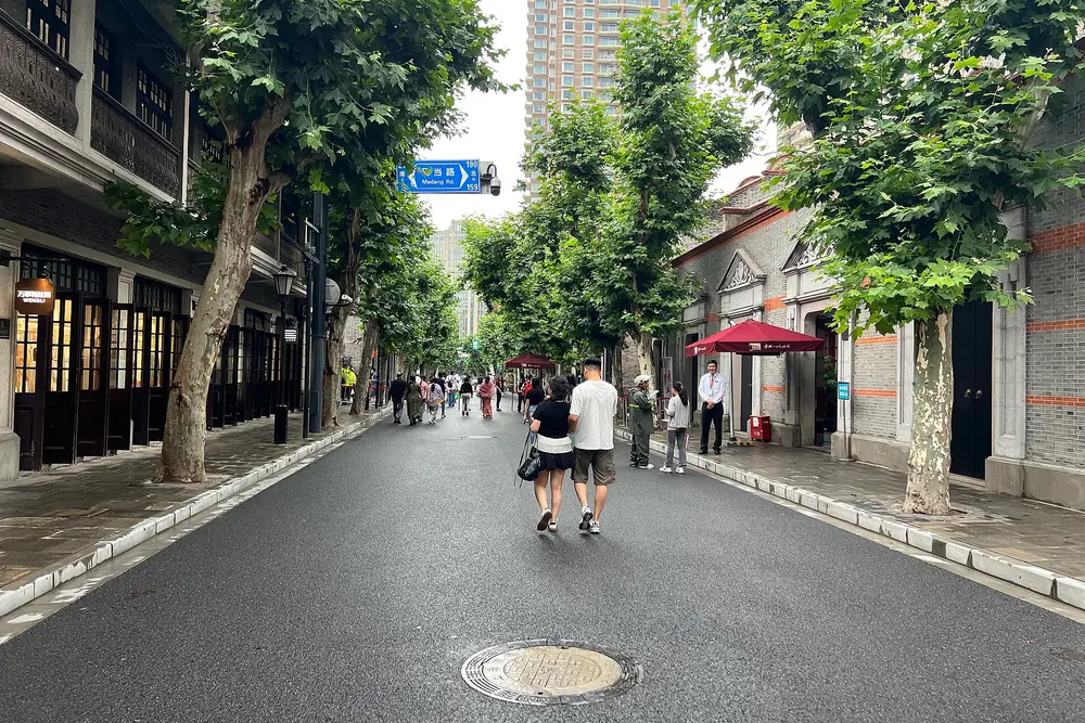 A quiet street lined with plane trees and grey-brick shikumen house fronts in Xintiandi, with a few people walking