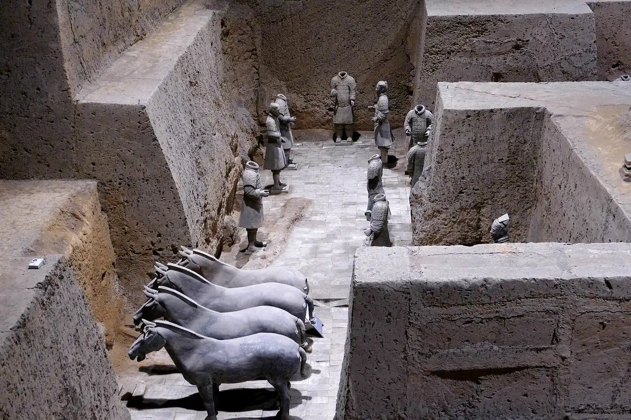 Four terracotta horses and a group of standing figures, several of them headless, in a small pit between high earth walls