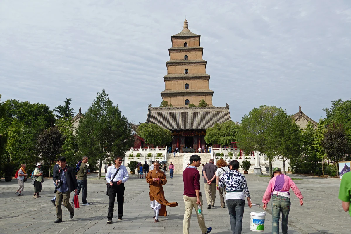 The square seven-tiered brick Big Wild Goose Pagoda rising behind a temple hall, with visitors and a monk crossing the plaza in front