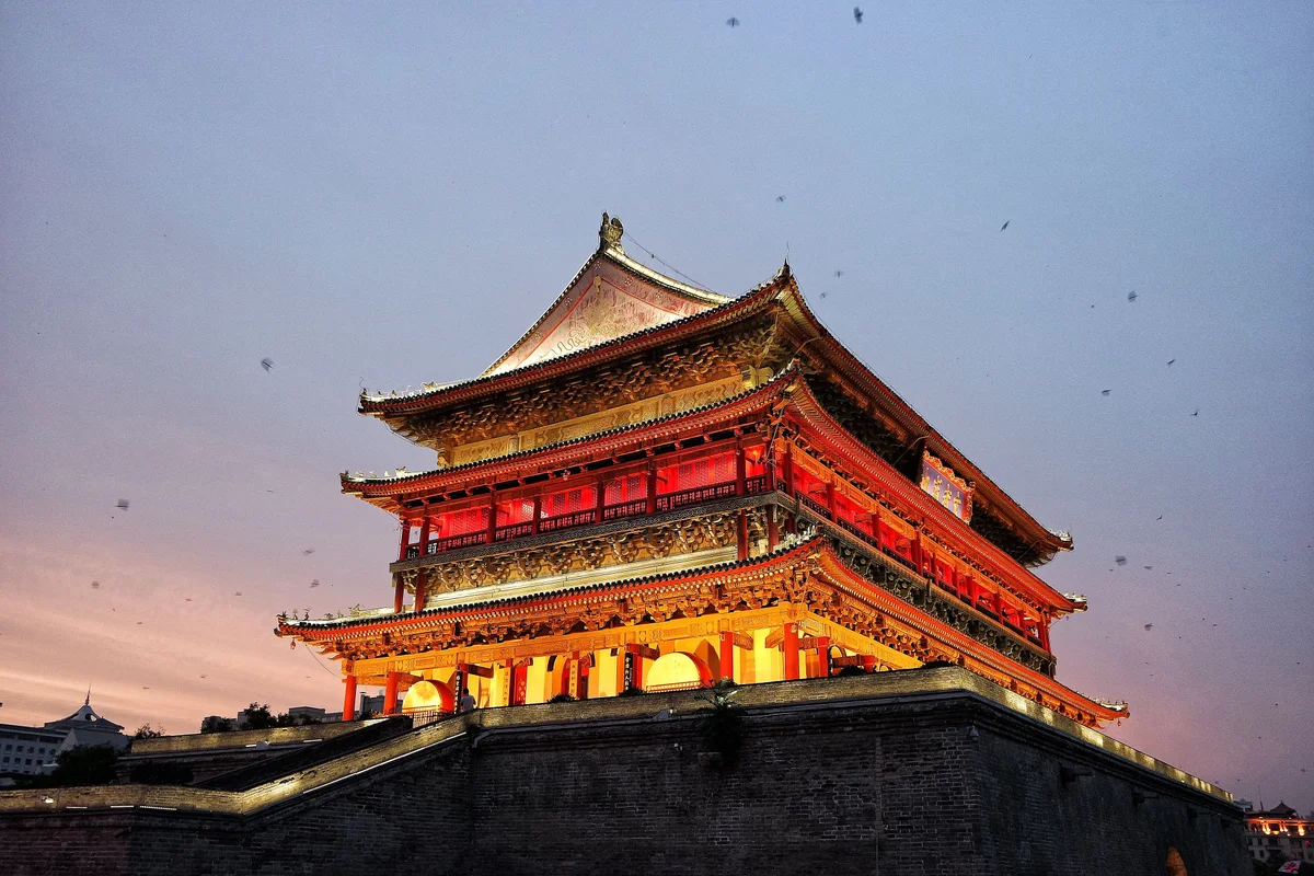 The Drum Tower lit gold and red from inside against a pink and violet evening sky, standing on its brick base