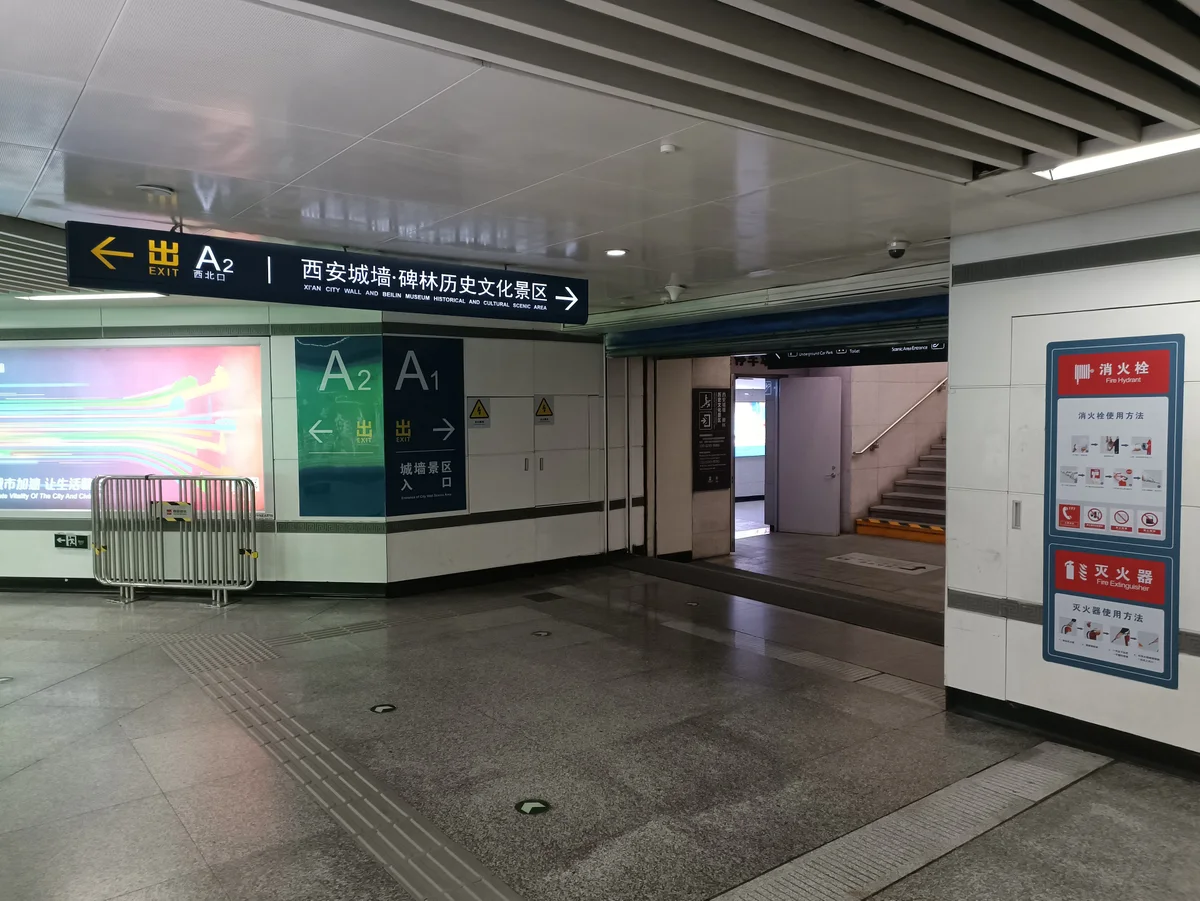 A metro concourse with overhead signs for exits A1 and A2 and a sign in Chinese and English pointing to the city wall and Beilin Museum scenic area